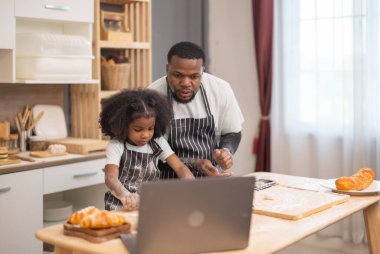 Un ve ekmek ruloları ile çevrili bir dizüstü bilgisayarı rehberlik etmek için birlikte yemek pişirmekten mutlu olan bir aile..