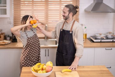 Güneşli mutfakta neşeli bir sahne, canlı bir atmosfer, çiftlerin çeşitli canlı meyvelerle eğlenceli bir etkileşim içinde olduğu bir yer. Oda sıcaklıkla, kahkahalarla, sevgi ve mutlulukla dolu.