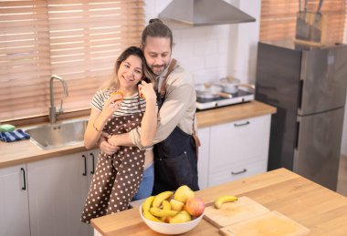 Güneşli mutfakta neşeli bir sahne, canlı bir atmosfer, çiftlerin çeşitli canlı meyvelerle eğlenceli bir etkileşim içinde olduğu bir yer. Oda sıcaklıkla, kahkahalarla, sevgi ve mutlulukla dolu.