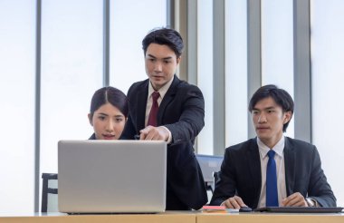 Bir grup iş adamı ofiste iş birliği yapıyor. Biri bilgisayar ekranına işaret ederken, diğerleri dikkatli bir şekilde, takım çalışmasını ve modern iş yerinde etkili iletişimi vurguluyor.