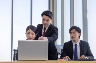 Bir grup iş adamı ofiste iş birliği yapıyor. Biri bilgisayar ekranına işaret ederken, diğerleri dikkatli bir şekilde, takım çalışmasını ve modern iş yerinde etkili iletişimi vurguluyor.