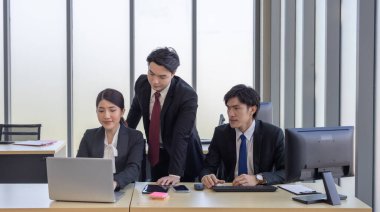 Bir grup iş adamı ofiste iş birliği yapıyor. Biri bilgisayar ekranına işaret ederken, diğerleri dikkatli bir şekilde, takım çalışmasını ve modern iş yerinde etkili iletişimi vurguluyor.