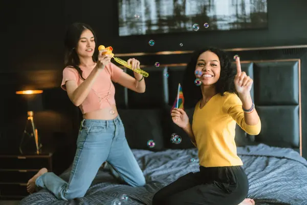 stock image An LGBT couple enjoys a playful moment blowing and chasing bubbles on a bed, exuding happiness and carefree fun. The scene is filled with vibrant colors and a sense of inclusivity.