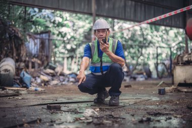 Bir güvenlik müfettişi endüstriyel bir ortamda petrol sızıntısını bildirmek için telsiz kullanıyor. Görüntü, karmaşık ve tehlikeli bir ortamda güvenliği sağlamanın kritik anını yakalıyor..