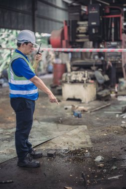 Bir güvenlik müfettişi endüstriyel bir ortamda petrol sızıntısını bildirmek için telsiz kullanıyor. Görüntü, karmaşık ve tehlikeli bir ortamda güvenliği sağlamanın kritik anını yakalıyor..