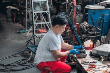 Kendini atölyeye adamış bir tamirci, güvenlik için eldiven giyerken araba kablolarını kontrol etmeye ve tamir etmeye odaklanmış. Otomotiv tamirinin doğası ve süreçteki detaylı bakım.