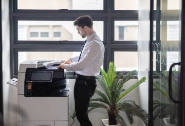 Profesyonel işadamı modern ofis ortamında fotokopi makinesi kullanıyor. Ofis görevlerinin verimliliği ve rutini, şirket ortamında belge yönetiminin önemini vurgulamak