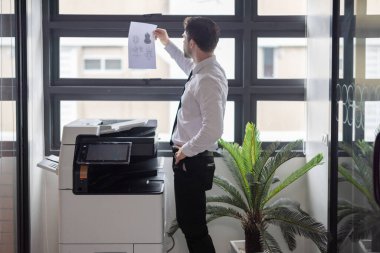 Profesyonel işadamı modern ofis ortamında fotokopi makinesi kullanıyor. Ofis görevlerinin verimliliği ve rutini, şirket ortamında belge yönetiminin önemini vurgulamak