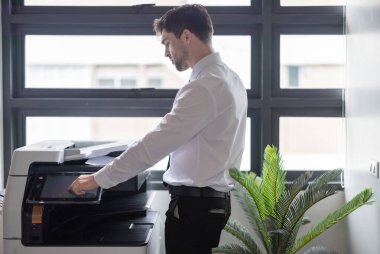 Profesyonel işadamı modern ofis ortamında fotokopi makinesi kullanıyor. Ofis görevlerinin verimliliği ve rutini, şirket ortamında belge yönetiminin önemini vurgulamak