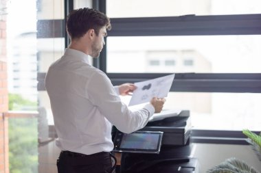 Profesyonel işadamı modern ofis ortamında fotokopi makinesi kullanıyor. Ofis görevlerinin verimliliği ve rutini, şirket ortamında belge yönetiminin önemini vurgulamak