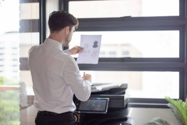 Profesyonel işadamı modern ofis ortamında fotokopi makinesi kullanıyor. Ofis görevlerinin verimliliği ve rutini, şirket ortamında belge yönetiminin önemini vurgulamak