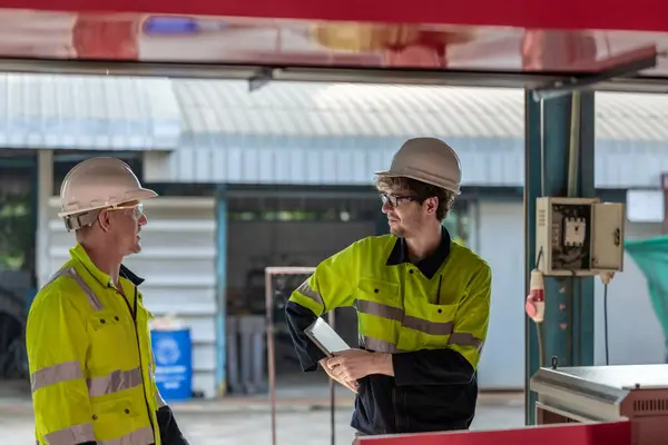 stock image Two robotic technicians in high visibility jackets and hard hats discuss operations in an industrial setting, emphasizing collaboration and safety in robotics maintenance facility and management.