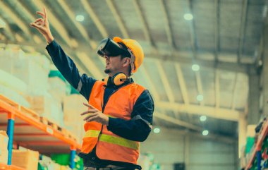 Modern depo ortamında dijital arayüzle etkileşime geçmek için sanal gerçeklik gözlüğü takan bir depo çalışanı. Gelişmiş teknolojinin lojistik ve envanter yönetimine entegrasyonu.