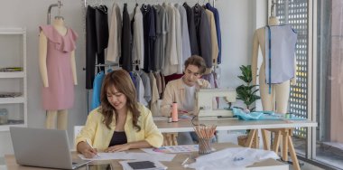 Moda tasarımcısı stüdyoda yeni kıyafet koleksiyonu için renk seçmeye odaklanmış durumda. Çalışma alanı yaratıcı araçlar, kumaş örnekleri, dikiş makinesi, canlı moda tasarım süreci ile dolu.