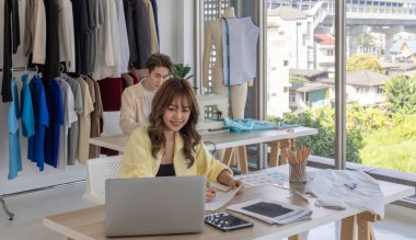 Moda tasarımcısı stüdyoda yeni kıyafet koleksiyonu için renk seçmeye odaklanmış durumda. Çalışma alanı yaratıcı araçlar, kumaş örnekleri, dikiş makinesi, canlı moda tasarım süreci ile dolu.