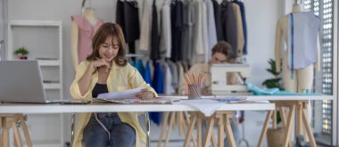 Moda tasarımcısı stüdyoda yeni kıyafet koleksiyonu için renk seçmeye odaklanmış durumda. Çalışma alanı yaratıcı araçlar, kumaş örnekleri, dikiş makinesi, canlı moda tasarım süreci ile dolu.