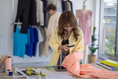 Moda tasarımcısı stüdyoda yeni kıyafet koleksiyonu için renk seçmeye odaklanmış durumda. Çalışma alanı yaratıcı araçlar, kumaş örnekleri, dikiş makinesi, canlı moda tasarım süreci ile dolu.