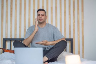 Sakin, loş bir yatak odasında, önünde dizüstü bilgisayarla meditasyon yapan bir adam ve yanında hafifçe parlayan bir mum, sakin ve odaklanmış bir atmosfer yaratıyor. Dijital detoks rutini