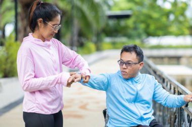 Tekerlekli sandalyede egzersiz yapan bir adam, bir direniş, güçlendirme ve kardiyo çalışması sırasında partneri tarafından destekleniyor. Bu resim fitness, motivasyon ve azim temalarını vurgular.