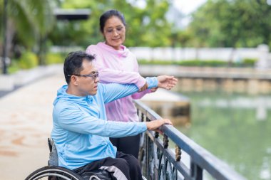 Tekerlekli sandalyede egzersiz yapan bir adam, bir direniş, güçlendirme ve kardiyo çalışması sırasında partneri tarafından destekleniyor. Bu resim fitness, motivasyon ve azim temalarını vurgular.