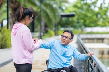 Tekerlekli sandalyede egzersiz yapan bir adam, bir direniş, güçlendirme ve kardiyo çalışması sırasında partneri tarafından destekleniyor. Bu resim fitness, motivasyon ve azim temalarını vurgular.
