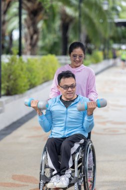 Tekerlekli sandalyede egzersiz yapan bir adam, bir direniş, güçlendirme ve kardiyo çalışması sırasında partneri tarafından destekleniyor. Bu resim fitness, motivasyon ve azim temalarını vurgular.