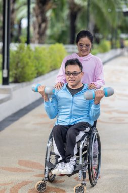 Tekerlekli sandalyede egzersiz yapan bir adam, bir direniş, güçlendirme ve kardiyo çalışması sırasında partneri tarafından destekleniyor. Bu resim fitness, motivasyon ve azim temalarını vurgular.