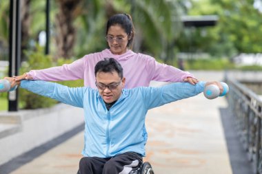 Tekerlekli sandalyede egzersiz yapan bir adam, bir direniş, güçlendirme ve kardiyo çalışması sırasında partneri tarafından destekleniyor. Bu resim fitness, motivasyon ve azim temalarını vurgular.