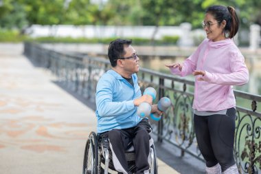 Tekerlekli sandalyede egzersiz yapan bir adam, bir direniş, güçlendirme ve kardiyo çalışması sırasında partneri tarafından destekleniyor. Bu resim fitness, motivasyon ve azim temalarını vurgular.