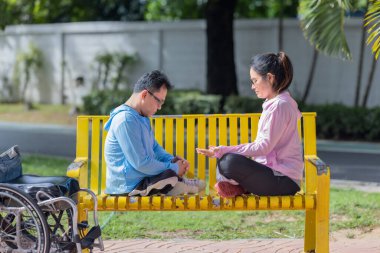 Bir çift, parkta sarı bir bankta huzurlu bir meditasyona girişiyor, dingin bir açık hava ortamında farkındalığı ve bağlantıyı teşvik ediyor..