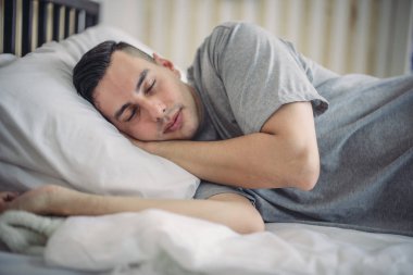 Karışık ırktan bir adam rahat, loş bir yatak odasında gece rutinini takip ederken görülüyor. Yatmaya hazırlanırken huzurlu bir atmosfer yakalıyor. Rahatlama ve sakinlik hissi yaratıyor..