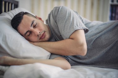 Karışık ırktan bir adam rahat, loş bir yatak odasında gece rutinini takip ederken görülüyor. Yatmaya hazırlanırken huzurlu bir atmosfer yakalıyor. Rahatlama ve sakinlik hissi yaratıyor..
