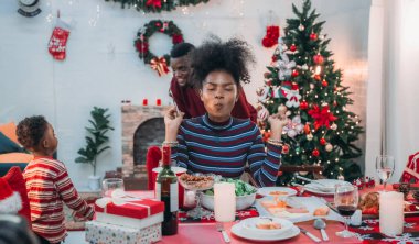 Siyah ailenin Noel yemeğinin keyfini çıkardığı canlı bir sahne, Noel mevsiminin sıcaklığını ve neşesini, güzel dekore edilmiş masaların etrafında yakalıyor, anne, baba ve oğulun özel anlarını paylaştığı.