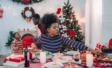 Siyah ailenin Noel yemeğinin keyfini çıkardığı canlı bir sahne, Noel mevsiminin sıcaklığını ve neşesini, güzel dekore edilmiş masaların etrafında yakalıyor, anne, baba ve oğulun özel anlarını paylaştığı.