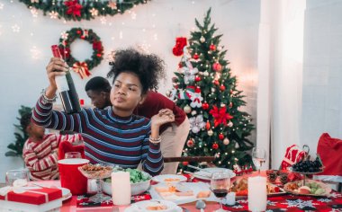 Siyah ailenin Noel yemeğinin keyfini çıkardığı canlı bir sahne, Noel mevsiminin sıcaklığını ve neşesini, güzel dekore edilmiş masaların etrafında yakalıyor, anne, baba ve oğulun özel anlarını paylaştığı.