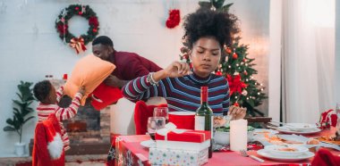Siyah ailenin Noel yemeğinin keyfini çıkardığı canlı bir sahne, Noel mevsiminin sıcaklığını ve neşesini, güzel dekore edilmiş masaların etrafında yakalıyor, anne, baba ve oğulun özel anlarını paylaştığı.