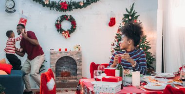 Siyah ailenin Noel yemeğinin keyfini çıkardığı canlı bir sahne, Noel mevsiminin sıcaklığını ve neşesini, güzel dekore edilmiş masaların etrafında yakalıyor, anne, baba ve oğulun özel anlarını paylaştığı.
