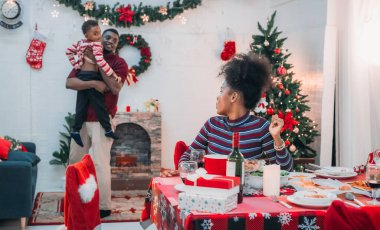 Siyah ailenin Noel yemeğinin keyfini çıkardığı canlı bir sahne, Noel mevsiminin sıcaklığını ve neşesini, güzel dekore edilmiş masaların etrafında yakalıyor, anne, baba ve oğulun özel anlarını paylaştığı.