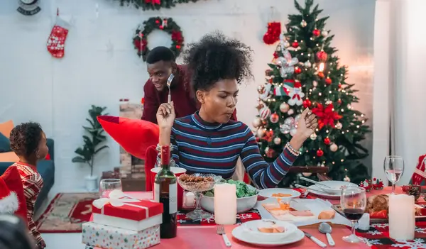 Siyah ailenin Noel yemeğinin keyfini çıkardığı canlı bir sahne, Noel mevsiminin sıcaklığını ve neşesini, güzel dekore edilmiş masaların etrafında yakalıyor, anne, baba ve oğulun özel anlarını paylaştığı.