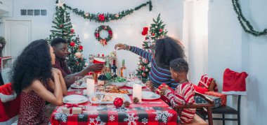Sıcak ve neşeli bir Noel yemeği sahnesi. Siyah aile sohbete daldı ve birlikte güzel süslenmiş Noel ağacı ve tatil masasıyla süslenmiş bayram yemeğinin tadını çıkardı.