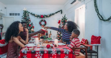 Sıcak ve neşeli bir Noel yemeği sahnesi. Siyah aile sohbete daldı ve birlikte güzel süslenmiş Noel ağacı ve tatil masasıyla süslenmiş bayram yemeğinin tadını çıkardı.