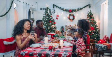 Sıcak ve neşeli bir Noel yemeği sahnesi. Siyah aile sohbete daldı ve birlikte güzel süslenmiş Noel ağacı ve tatil masasıyla süslenmiş bayram yemeğinin tadını çıkardı.