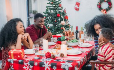 Sıcak ve neşeli bir Noel yemeği sahnesi. Siyah aile sohbete daldı ve birlikte güzel süslenmiş Noel ağacı ve tatil masasıyla süslenmiş bayram yemeğinin tadını çıkardı.
