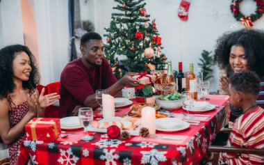 Sıcak ve neşeli bir Noel yemeği sahnesi. Siyah aile sohbete daldı ve birlikte güzel süslenmiş Noel ağacı ve tatil masasıyla süslenmiş bayram yemeğinin tadını çıkardı.
