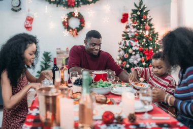 Sıcak ve neşeli bir Noel yemeği sahnesi. Siyah aile sohbete daldı ve birlikte güzel süslenmiş Noel ağacı ve tatil masasıyla süslenmiş bayram yemeğinin tadını çıkardı.