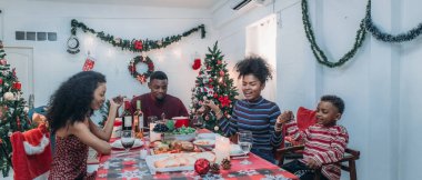 Sıcak ve neşeli bir Noel yemeği sahnesi. Siyah aile sohbete daldı ve birlikte güzel süslenmiş Noel ağacı ve tatil masasıyla süslenmiş bayram yemeğinin tadını çıkardı.