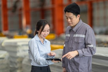 Profesyonel bir erkek ve kadın dijital tablet üzerinde iş birliği yaparak, sürdürülebilir iyileştirme için ISO standartlarını yükseltmek için bir metal levha fabrikasının hareketli ortamında iş birliği yapıyorlar..