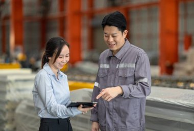 Profesyonel bir erkek ve kadın dijital tablet üzerinde iş birliği yaparak, sürdürülebilir iyileştirme için ISO standartlarını yükseltmek için bir metal levha fabrikasının hareketli ortamında iş birliği yapıyorlar..