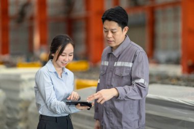 Profesyonel bir erkek ve kadın dijital tablet üzerinde iş birliği yaparak, sürdürülebilir iyileştirme için ISO standartlarını yükseltmek için bir metal levha fabrikasının hareketli ortamında iş birliği yapıyorlar..