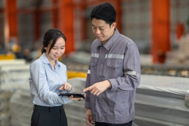 Profesyonel bir erkek ve kadın dijital tablet üzerinde iş birliği yaparak, sürdürülebilir iyileştirme için ISO standartlarını yükseltmek için bir metal levha fabrikasının hareketli ortamında iş birliği yapıyorlar..